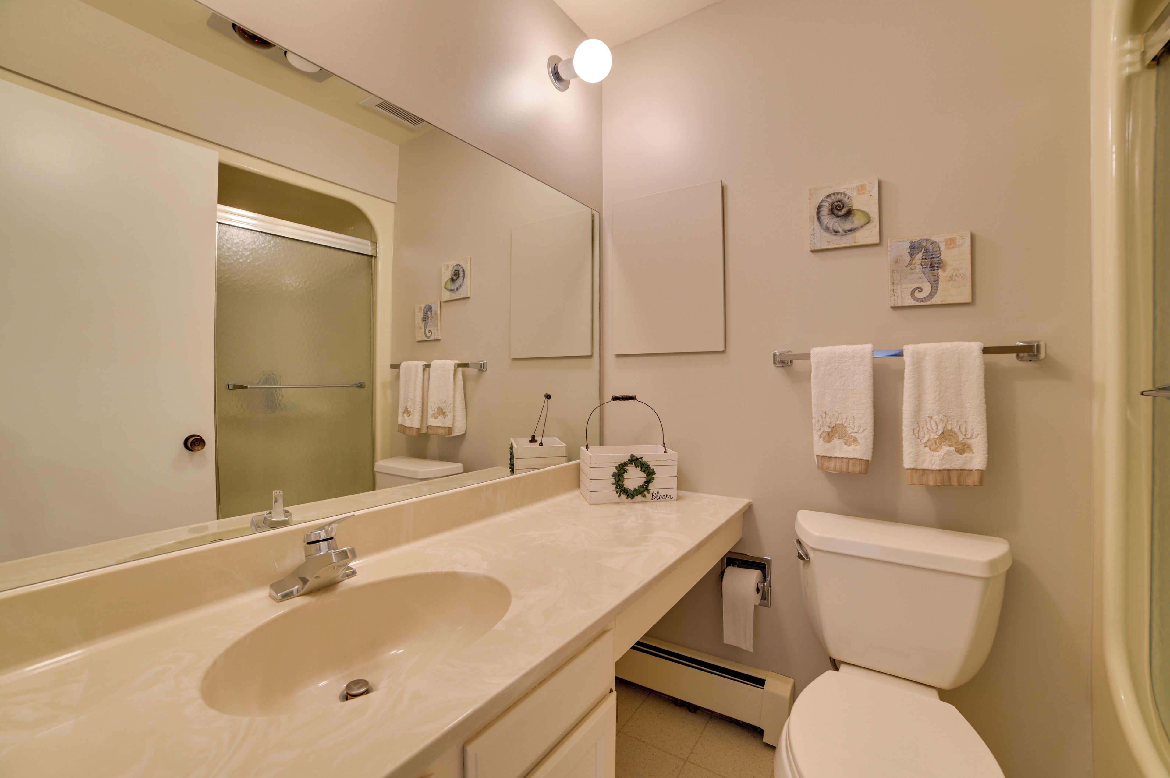 A bathroom with a large mirror, a sink, a toilet, and towels on a rack.