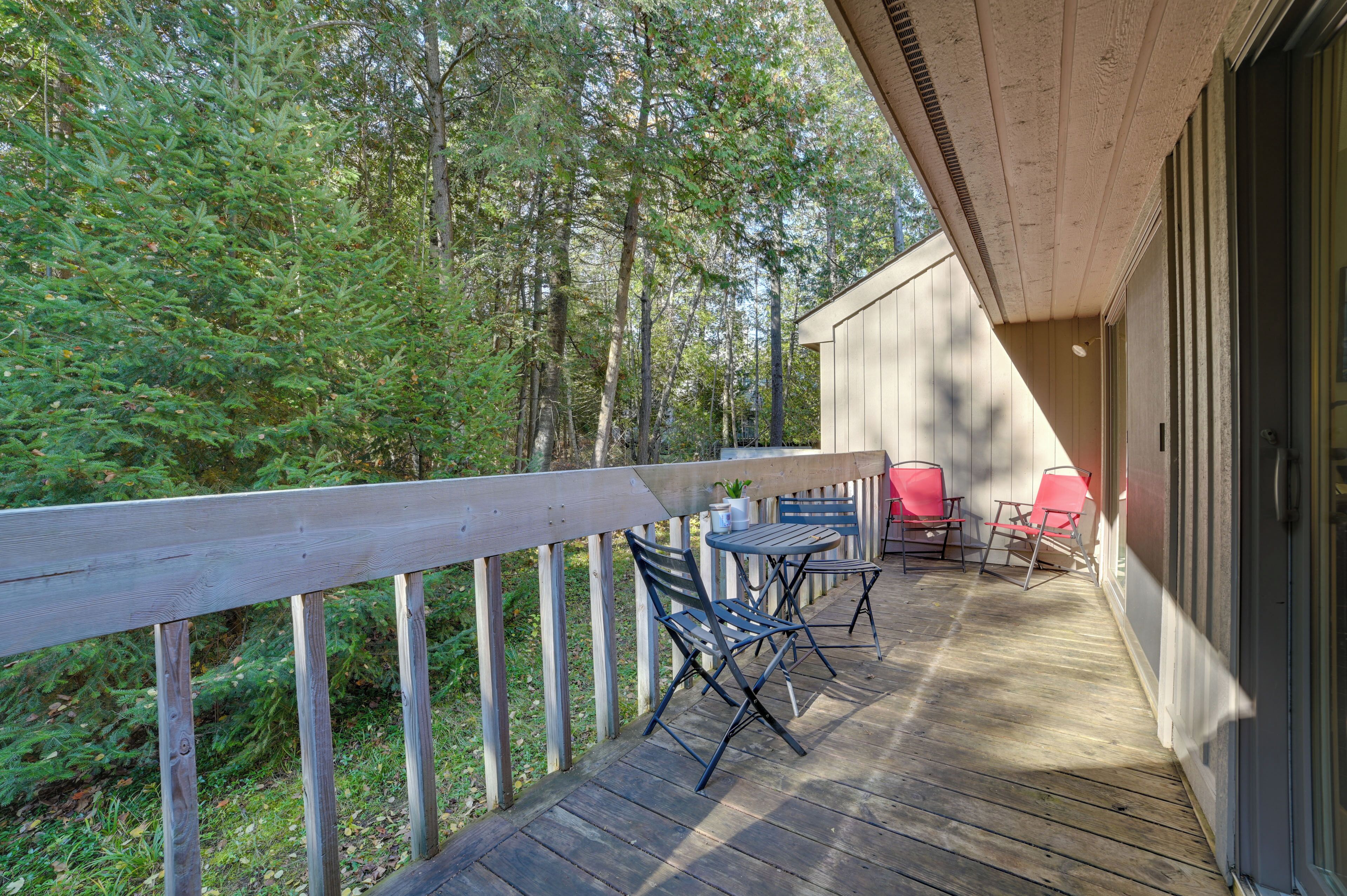 A wooden deck with a railing, outdoor seating, and a view of a forest.