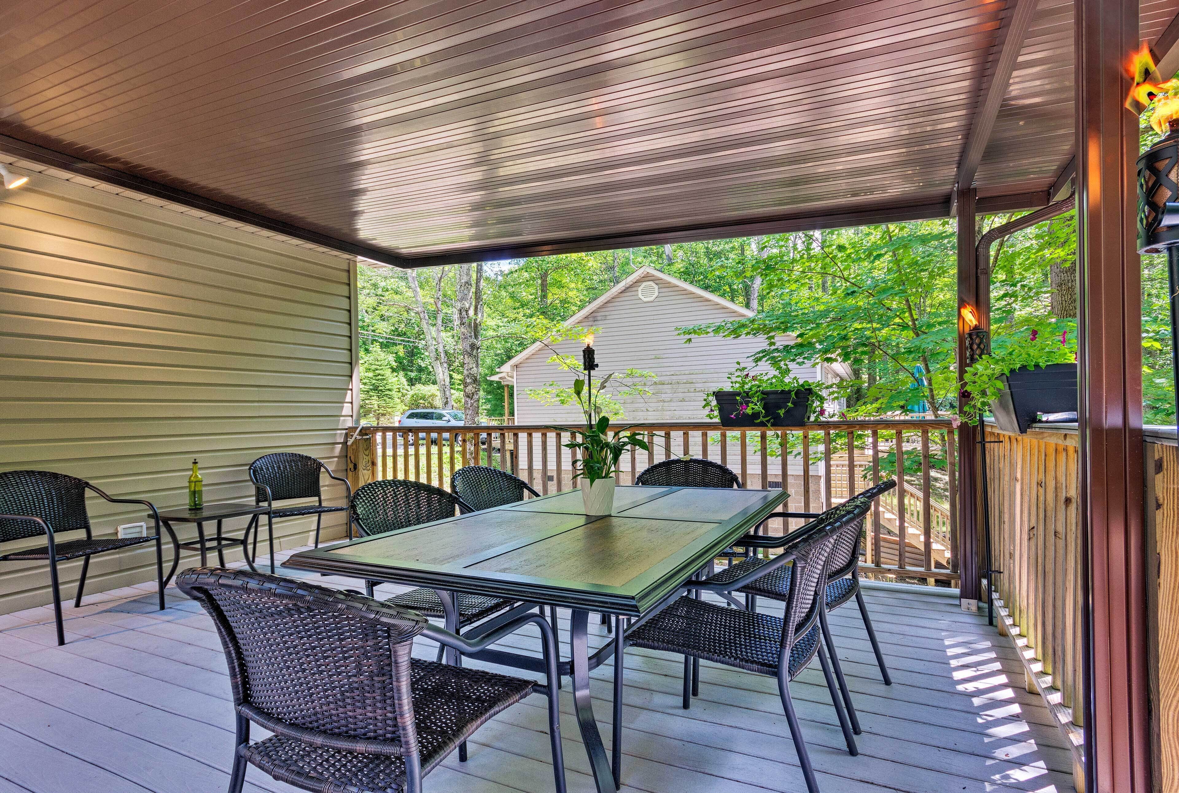 A covered patio with a table and chairs, a potted plant, and a view of a house and trees.