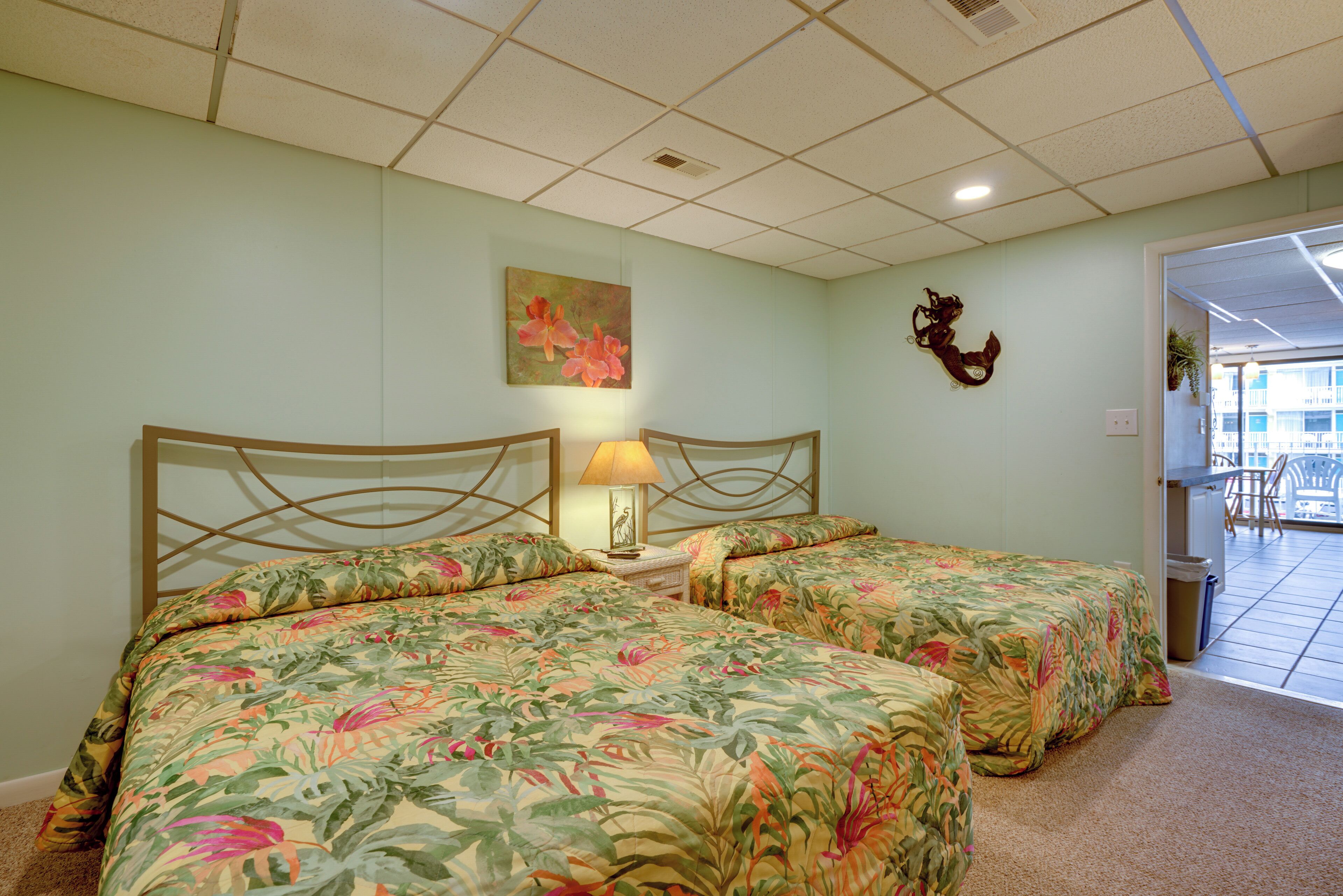 Ein Hotelzimmer mit zwei Betten, einem Nachttisch mit Lampe, einem floralen Bild an der Wand und einem dekorativen Gegenstand über dem Bett.