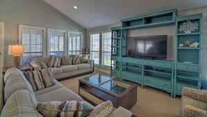Een woonkamer met een grote televisie, een entertainmentmeubel in blauwgroen en een bank met gestreepte kussens.