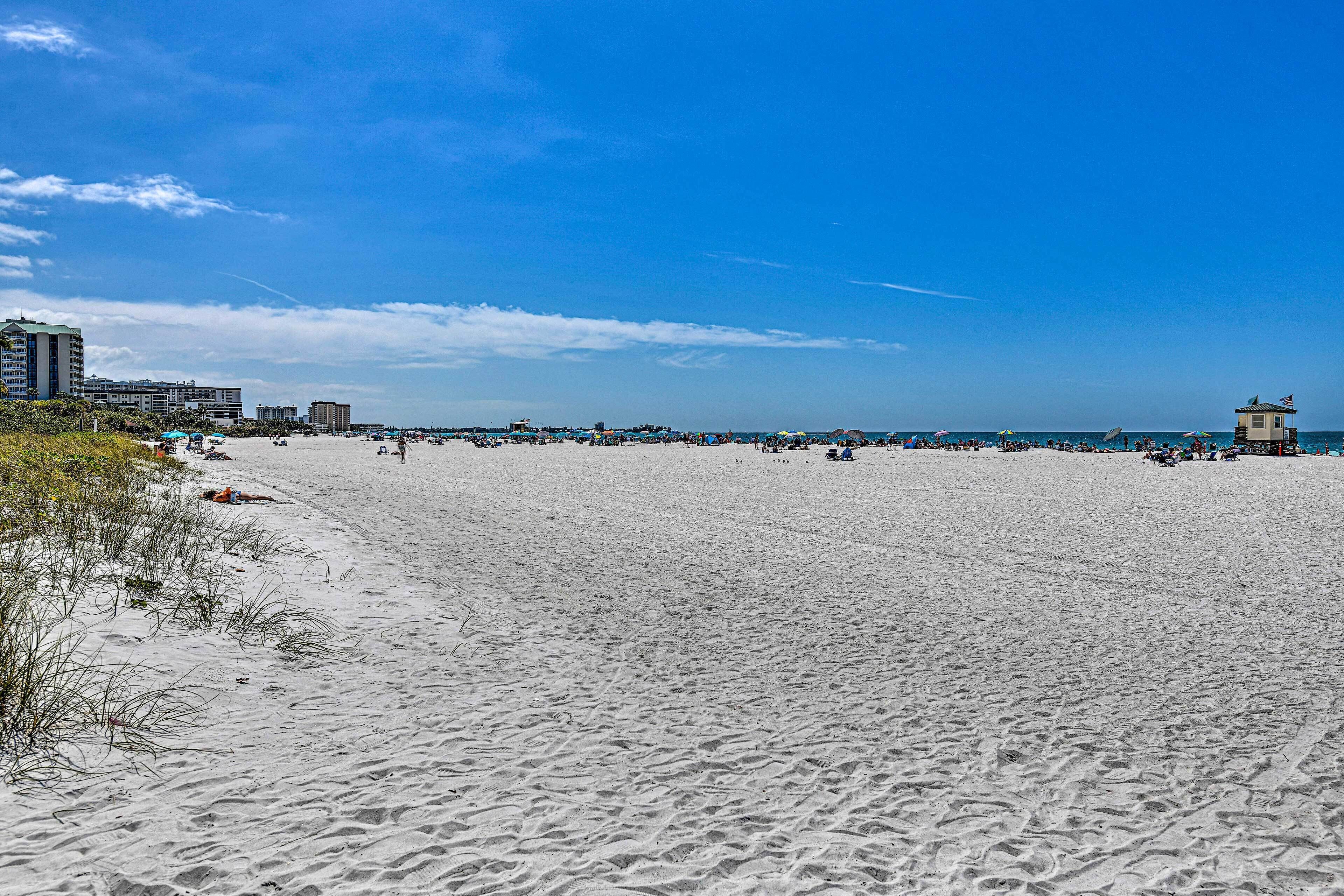 A wide sandy beach with a clear sky and distant buildings.