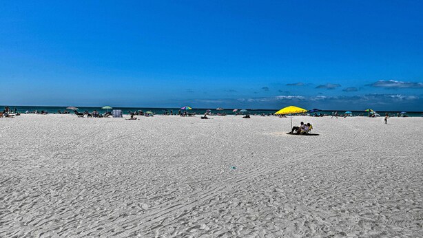 A wide sandy beach with a few umbrellas and people.