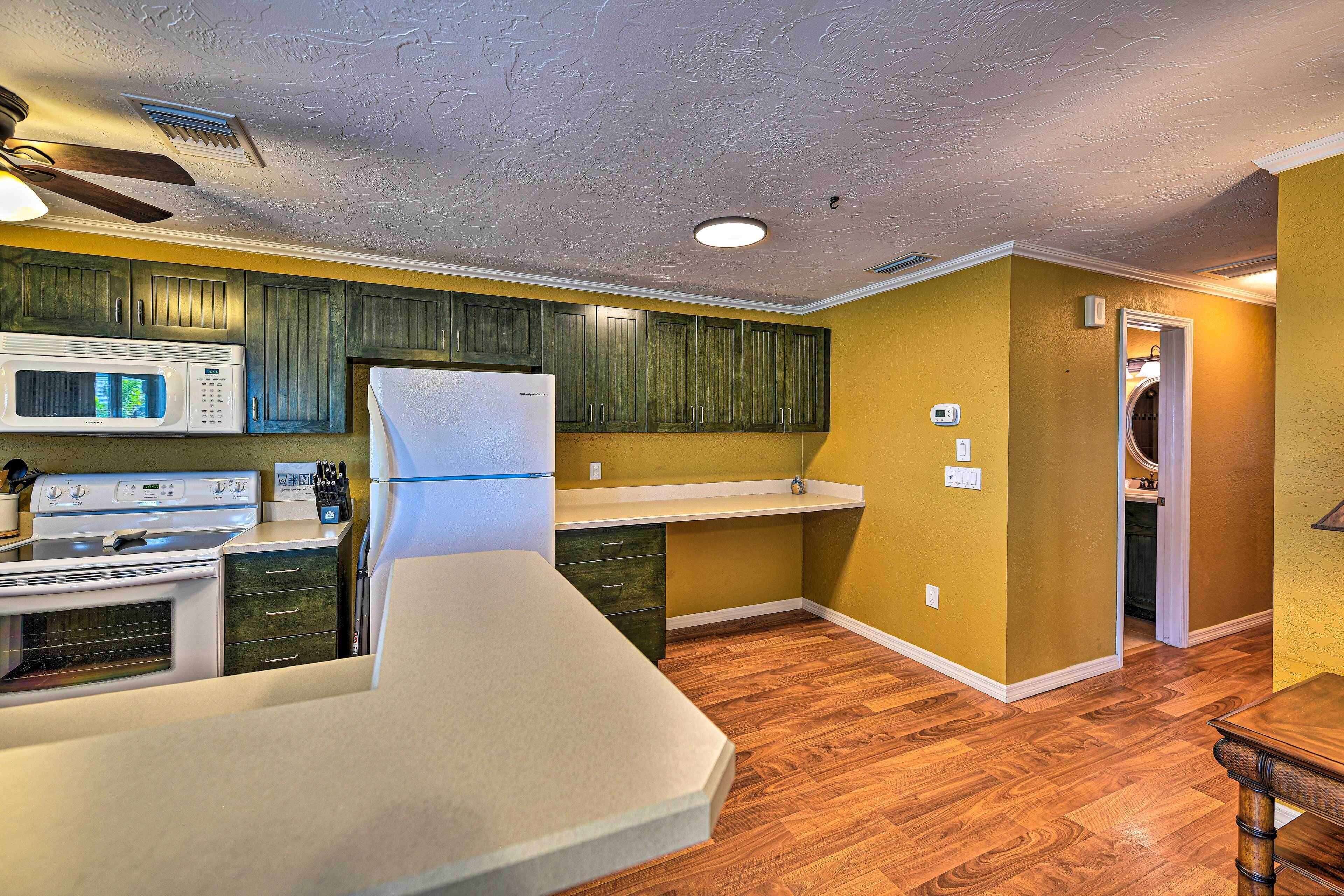 A compact kitchen with a microwave, stove, refrigerator, and wooden cabinets.