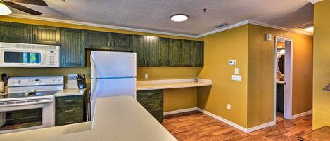A compact kitchen with a microwave, stove, refrigerator, and wooden cabinets.