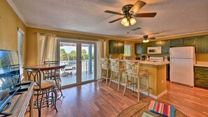 A kitchen with a dining area, wooden flooring, a ceiling fan, and a view through the glass door.