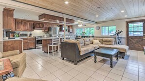 A spacious living area with a sofa, a coffee table, and a dining table. There is a kitchen area with wooden cabinets and a refrigerator.