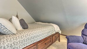 A bedroom with a bed, pillows, a blanket, and a chair.