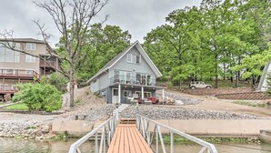 A two-story house with a balcony, a dock leading to a body of water, and a vehicle parked nearby.
