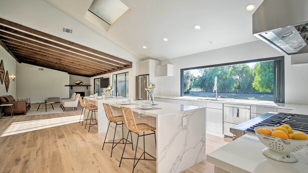 A modern kitchen with a large island, bar stools, and a view of the outdoors.