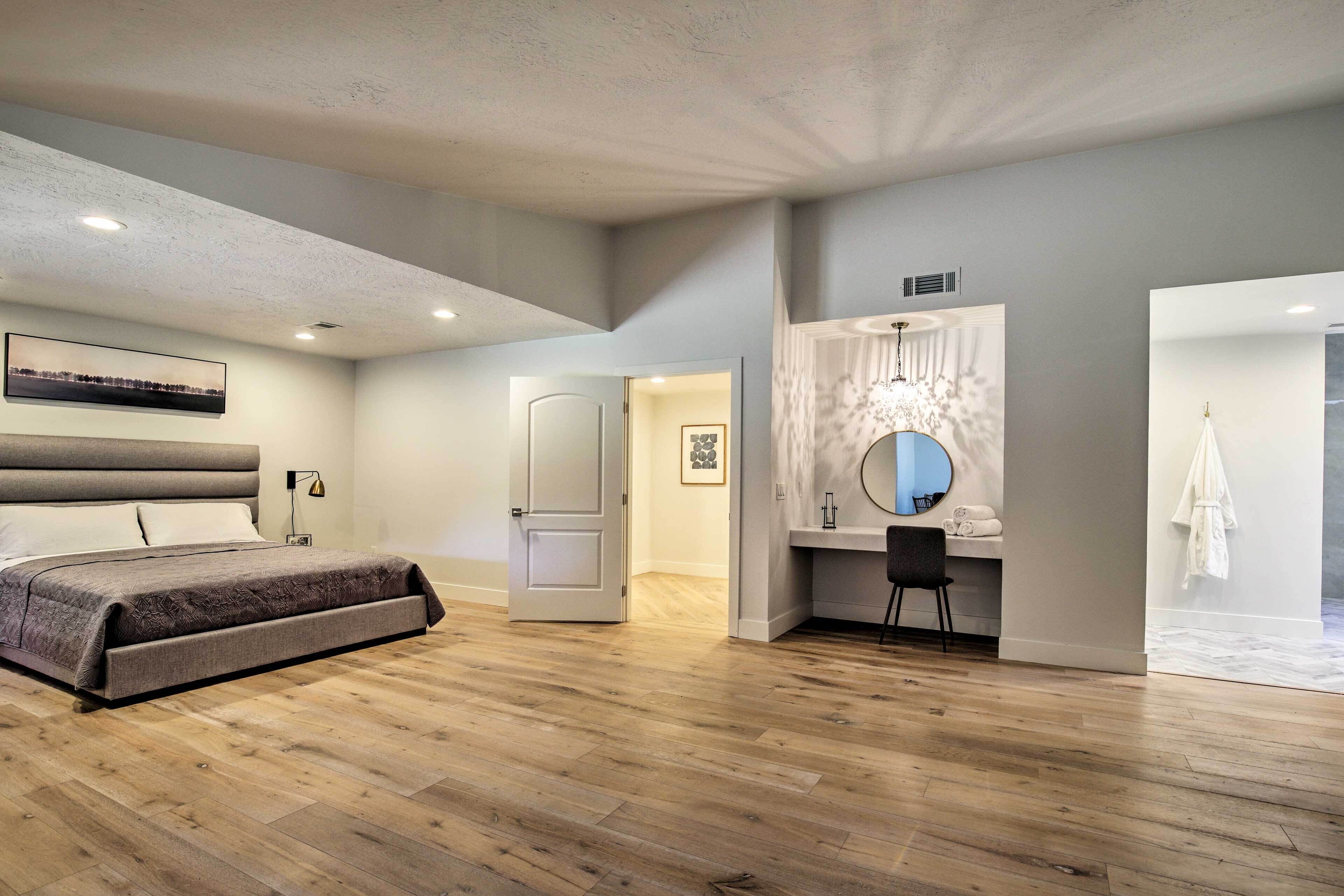 Un dormitorio moderno con una cama grande, un tocador con espejo y una puerta que conduce a otra habitación.