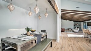 A modern dining area with a wooden table set for four, a bench, and hanging pendant lights.