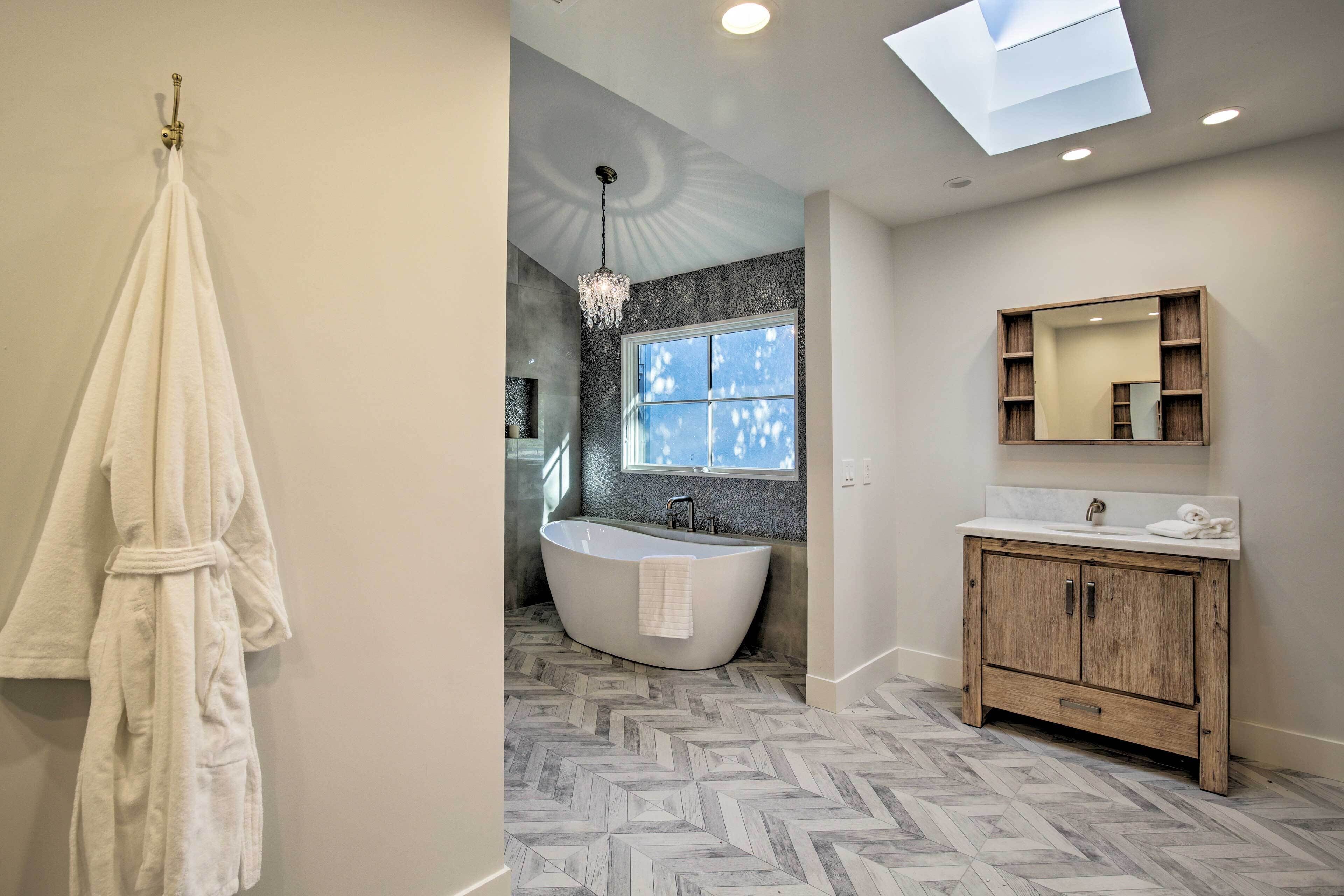 Une salle de bain moderne avec une baignoire îlot, un meuble-lavabo avec miroir et un sol décoré d’un motif en chevrons.