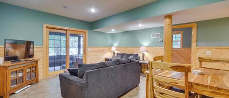 A living room with a sofa, TV, wooden furniture, and a dining area.