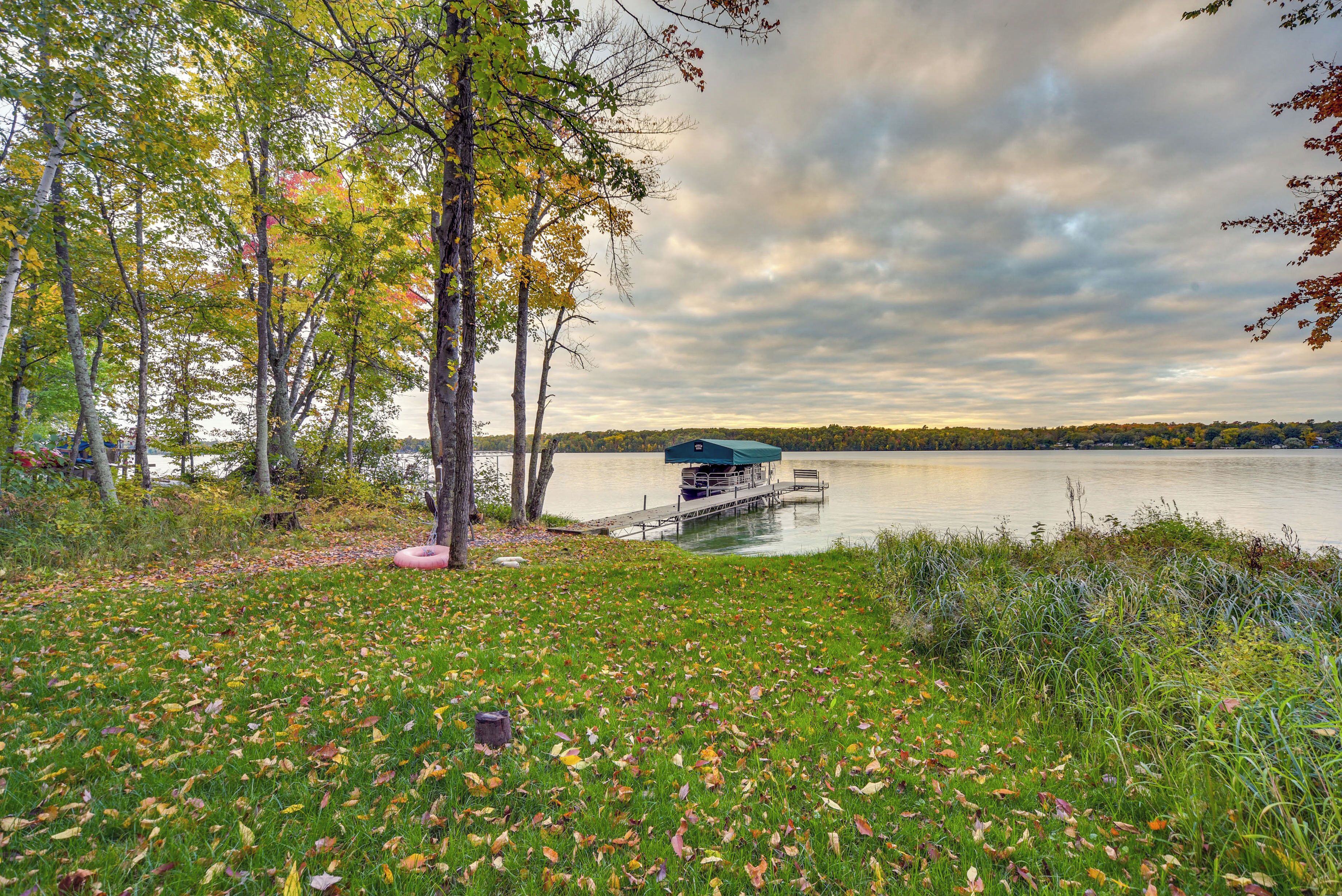 A lakeside dock with a covered seating area, surrounded by trees and grassy banks.
