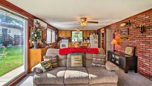 A cozy living room with a large window, a ceiling fan, and a brick wall with a welcome sign.