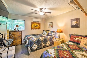 A bedroom with two beds, a ceiling fan, a dresser, a chair, and a window with a view of trees. - Cozy Waterfront Cottage w/ Deck on White River! (Cotter)