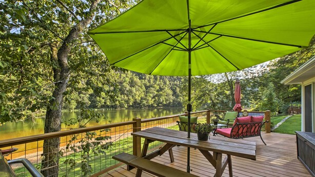 A wooden deck with a picnic table and chairs, overlooking a lake.