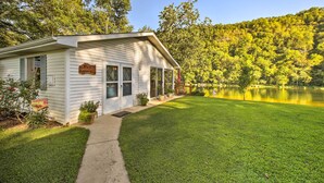A white cabin labeled "Wildcat Cottage" with a covered porch, a well-maintained lawn, and a lake in the background.