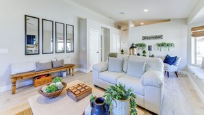 A modern living room with a white sofa, a wooden bench, and a coffee table with decorative items. - Updated Gilbert Home w/ Covered Patio (Gilbert)