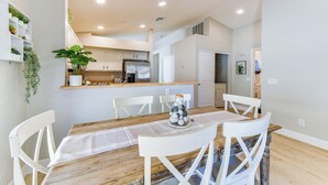 A dining area with a wooden table and white chairs, a kitchen in the background, and a plant on the wall. - Updated Gilbert Home w/ Covered Patio (Gilbert)