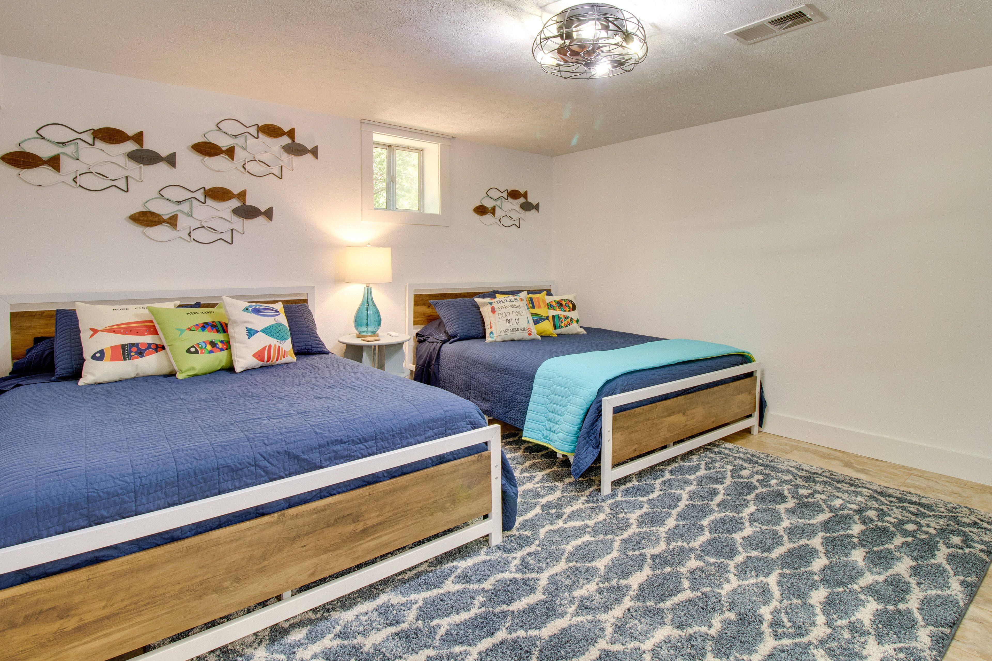 A bedroom with two beds, a patterned rug, wall art, a window, and a lamp.