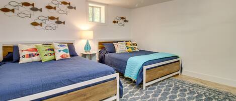 A bedroom with two beds, a patterned rug, wall art, a window, and a lamp.