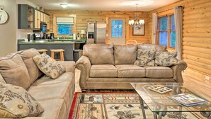 A cozy cabin interior with a living room featuring a leather sofa and a glass coffee table, a kitchen with modern appliances, and wooden walls. - Cedar Mountain Log Cabin: 4 Mi Dupont State Forest (Brevard)