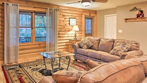 A log cabin interior with a leather sofa, a glass coffee table, and a ceiling fan. - Cedar Mountain Log Cabin: 4 Mi Dupont State Forest (Brevard)