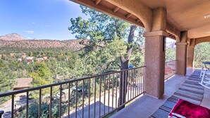 Ein Balkon mit Blick auf eine gebirgige Landschaft, einer Pergola und einer roten Decke am Boden.