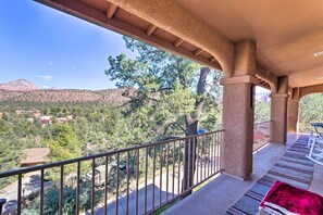 Un balcón con vistas a un paisaje montañoso, una estructura de pérgola y una manta roja en el suelo.