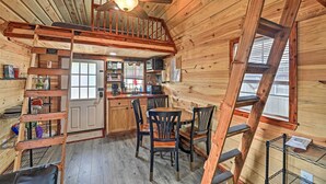 A wooden cabin interior with a dining area, kitchen, and loft bedroom. - 'the Gosling' Studio Cabin w/ River Access! (New Bern)