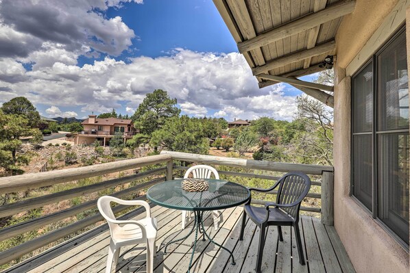 A wooden deck with a round table and chairs, overlooking a desert landscape with houses and trees.