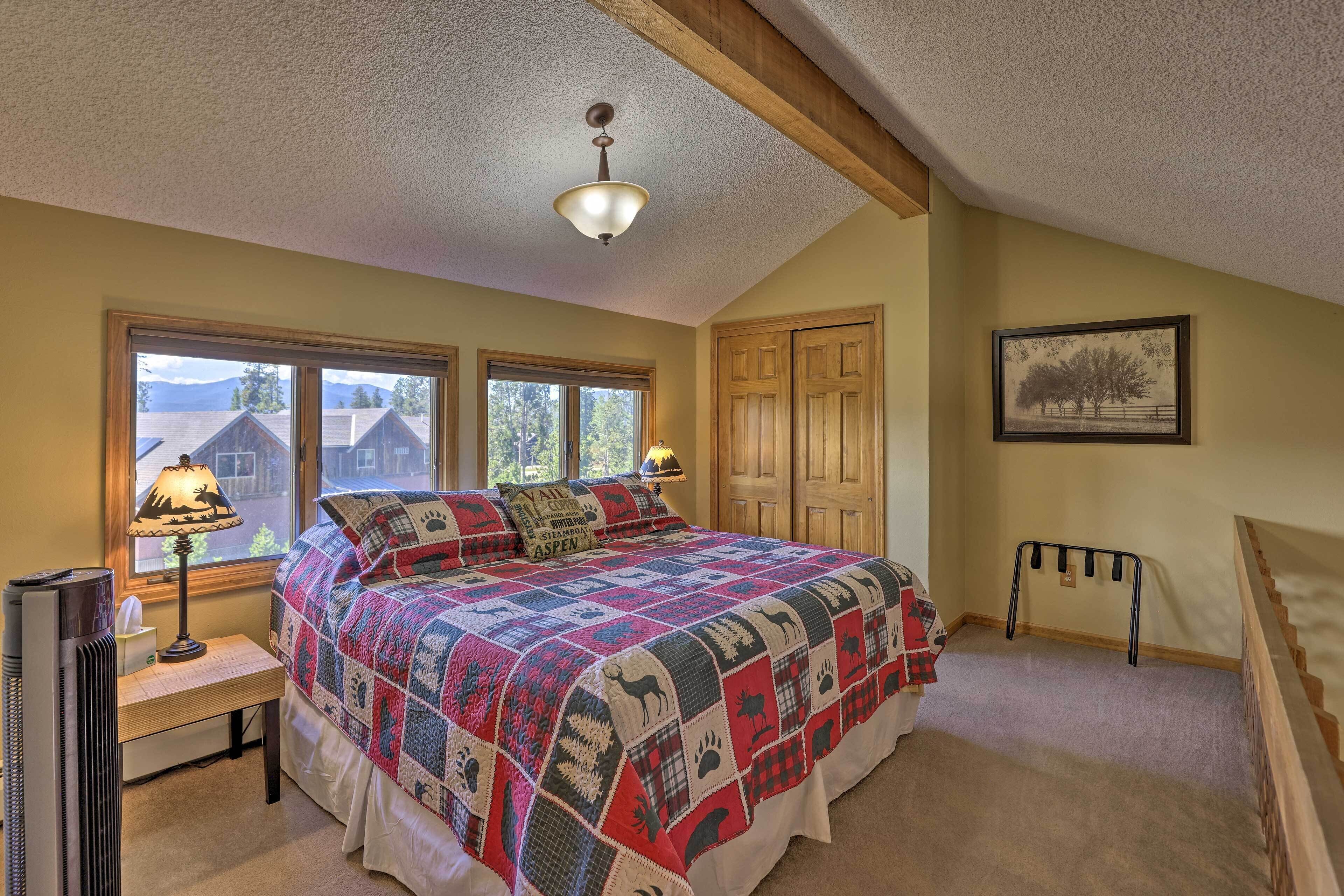 A bedroom with a large bed, a window with a view, a ceiling fan, and a framed picture on the wall.