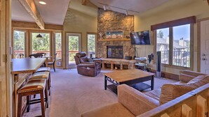 A spacious living area with a stone fireplace, leather furniture, and large windows offering a view of the outdoors. - Townhome w/ Club Access on Shuttle Stop (Fraser)
