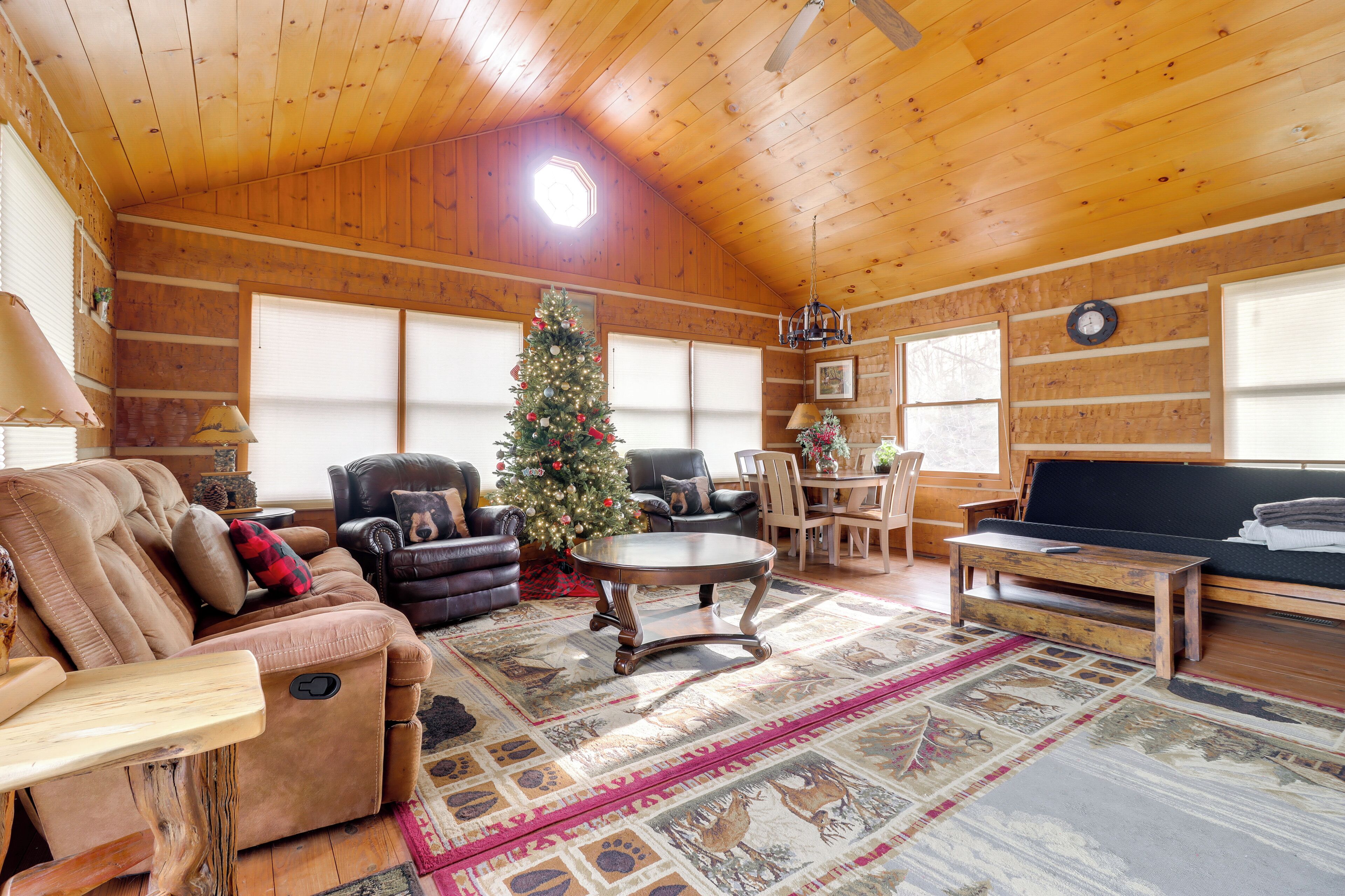 A cozy log cabin interior with a leather sofa, a coffee table, a Christmas tree, and a dining area.