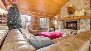 L’intérieur chaleureux d’un chalet avec un canapé en cuir, un sapin de Noël, une cheminée en pierre et des murs en bois.