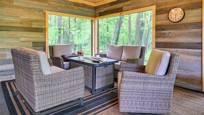Une pièce chaleureuse, meublée de mobilier en osier, avec un plafond en bois et de grandes fenêtres donnant sur la forêt.