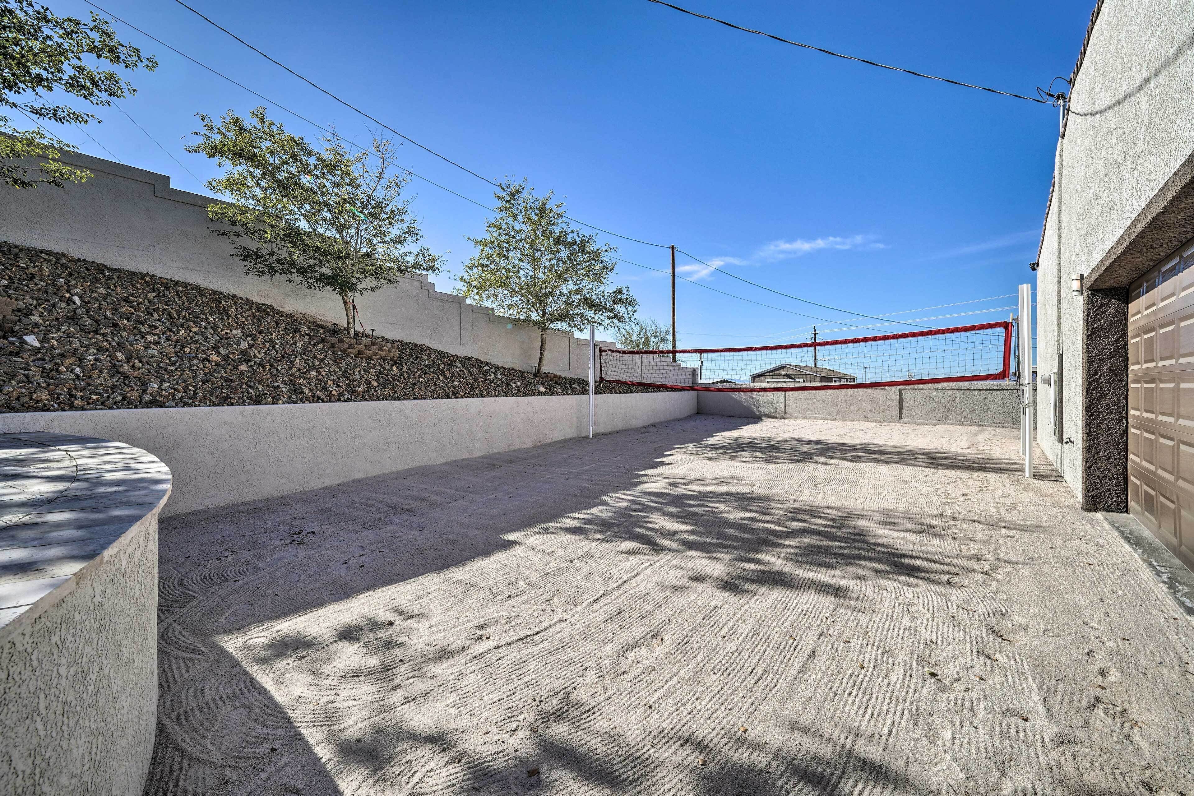 A sandy volleyball court with a red net, surrounded by a concrete wall and trees.