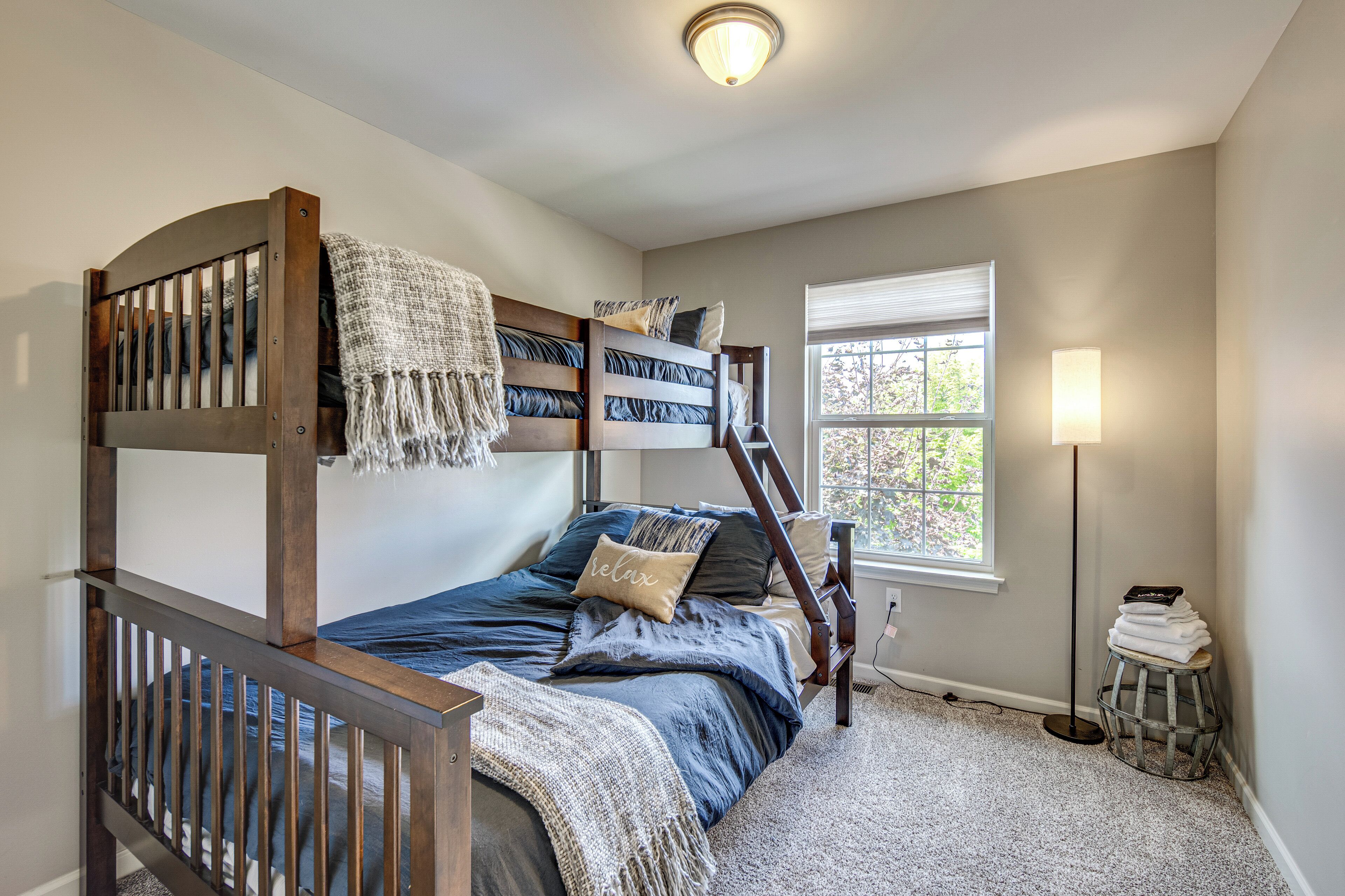 A bunk bed room with a window, a lamp, and a small stool.