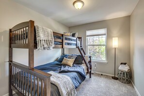 A bunk bed room with a window, a lamp, and a small stool.
