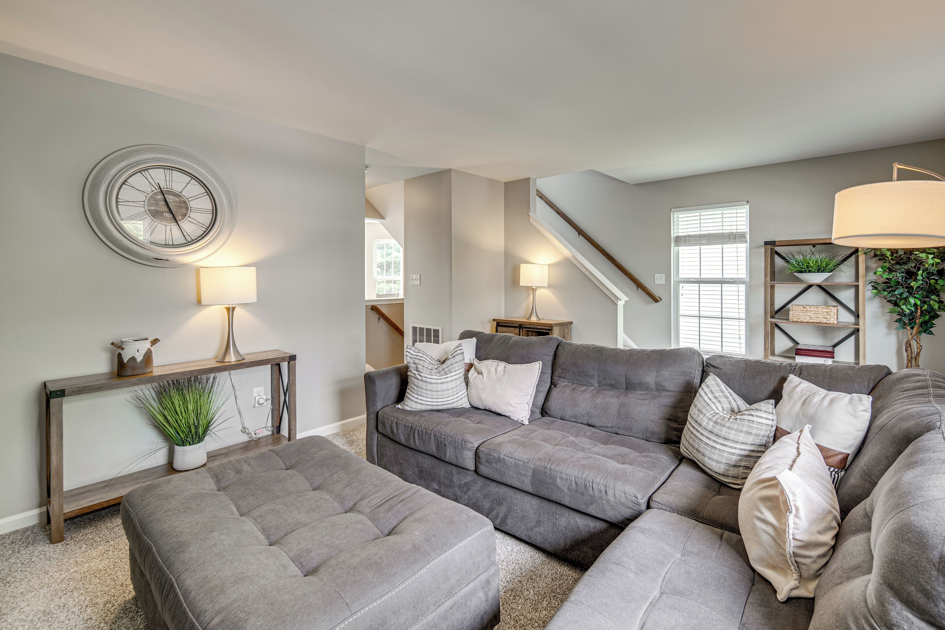 A living room with a sectional sofa, a round wall clock, and a staircase leading to another level.