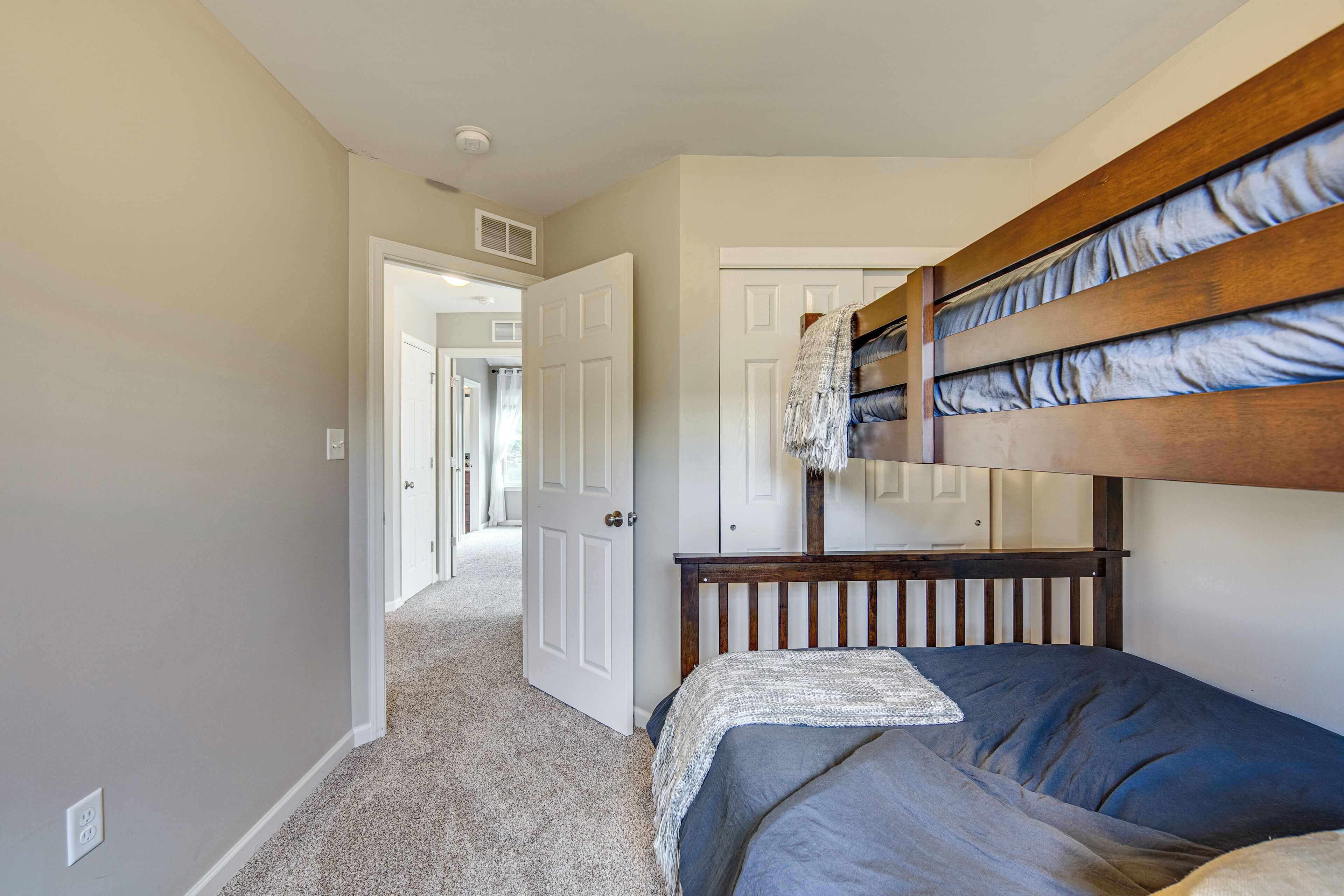 A room with a bunk bed, carpeted floor, white walls, and a door leading to another room.