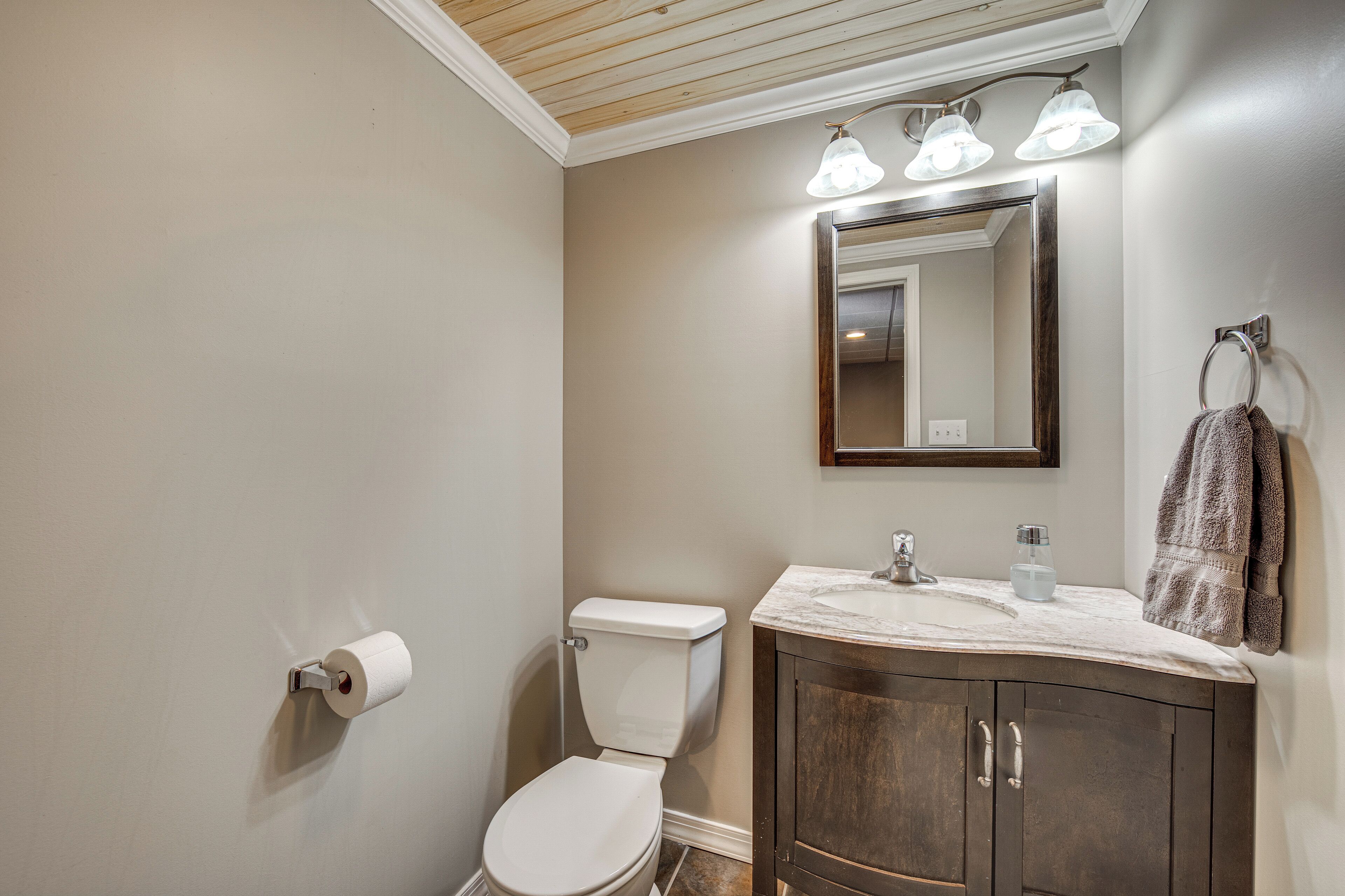 A bathroom with a toilet, sink, mirror, towel rack, and toilet paper.