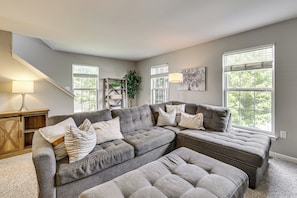 A living room with a sectional sofa, a lamp, a plant, and artwork on the walls. - Charming Bellefonte Townhome Near Penn State! (Bellefonte)