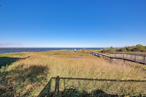 A boardwalk leading to a dock over a marshy area with a clear view of the water and distant land.