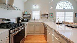 Una cucina moderna con piano cottura in acciaio inossidabile, mobili bianchi e un'ampia finestra con persiane.