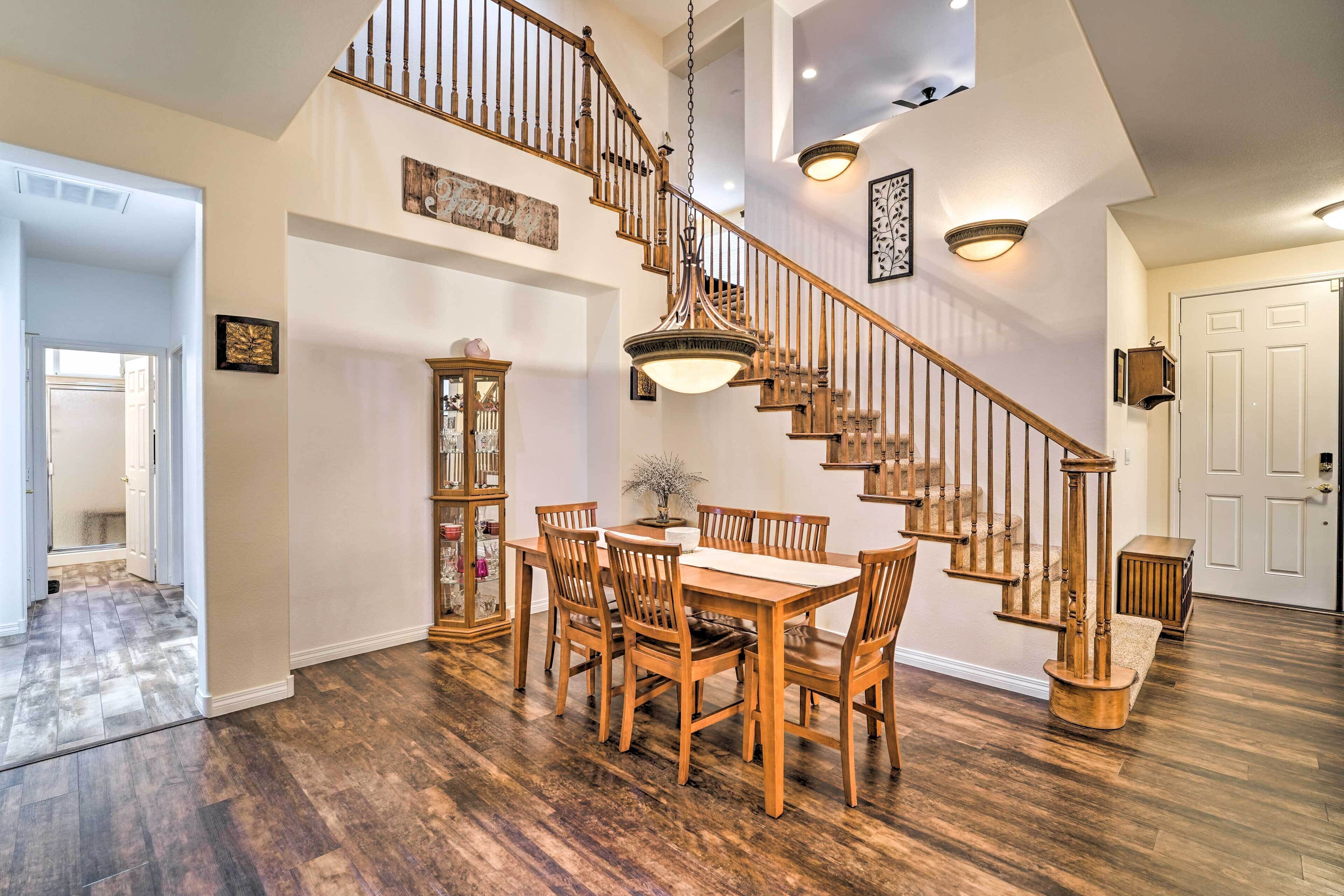A spacious dining area with a wooden table and chairs, a staircase with wooden railings, and a hanging light fixture.