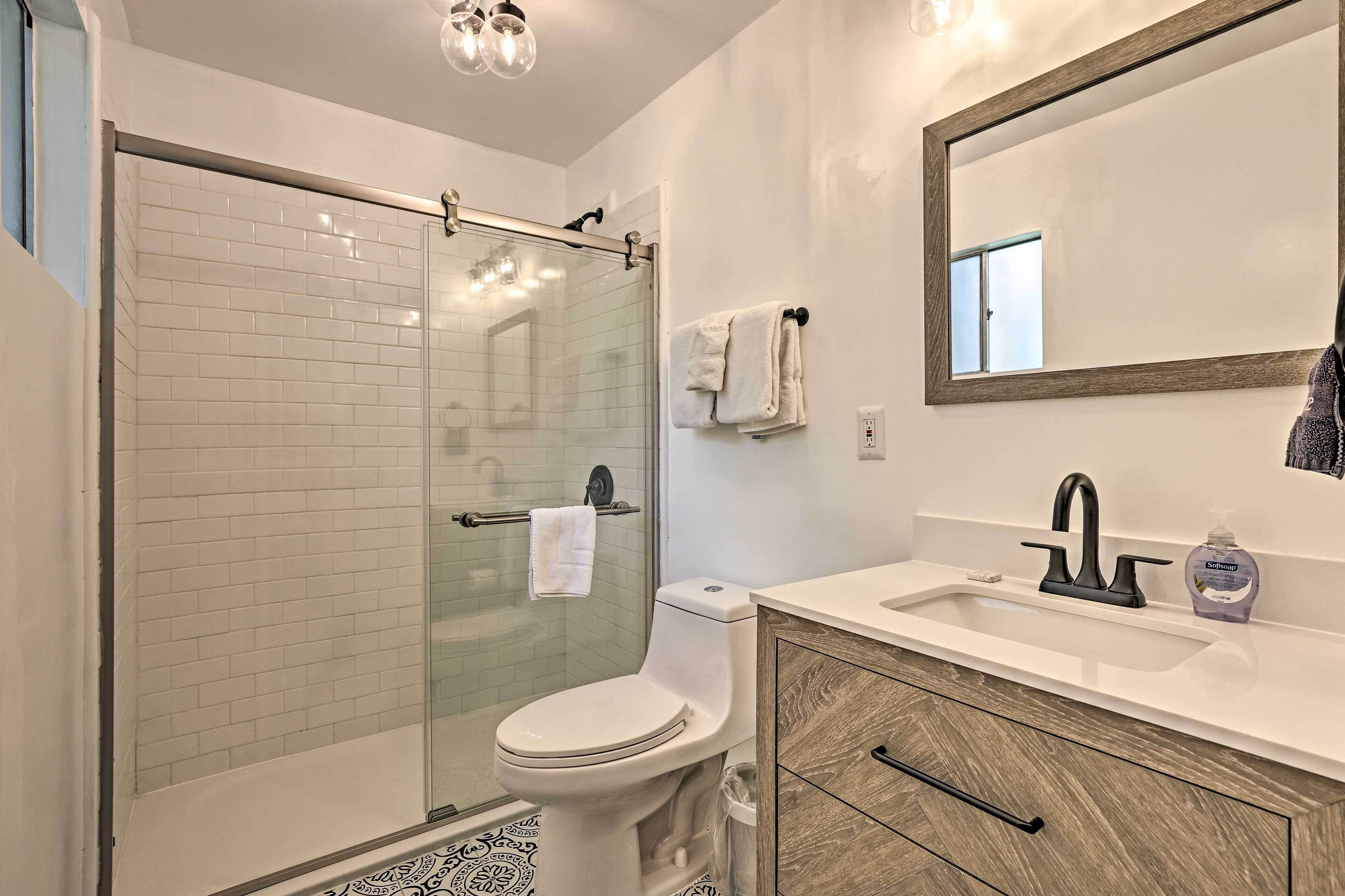 A modern bathroom with a glass shower enclosure, a toilet, a sink with a soap dispenser, and a mirror above the sink.