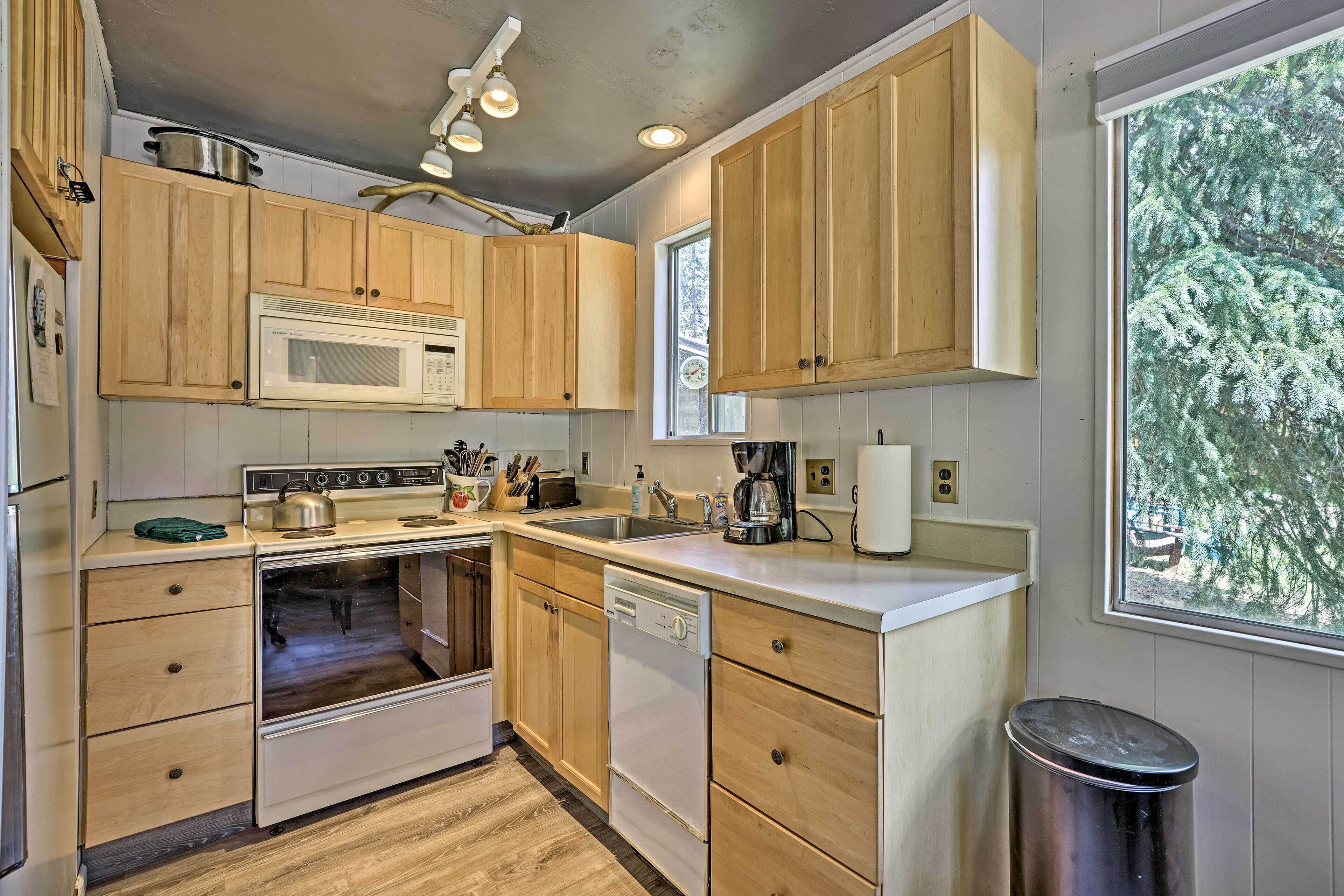 A kitchen with wooden cabinets, a microwave, an oven, a dishwasher, and a window with a view of trees.